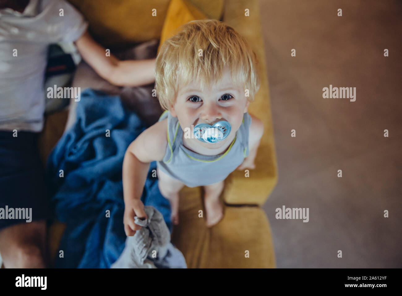 Little boy with pacifier standing on couch, looking up at camera Stock ...