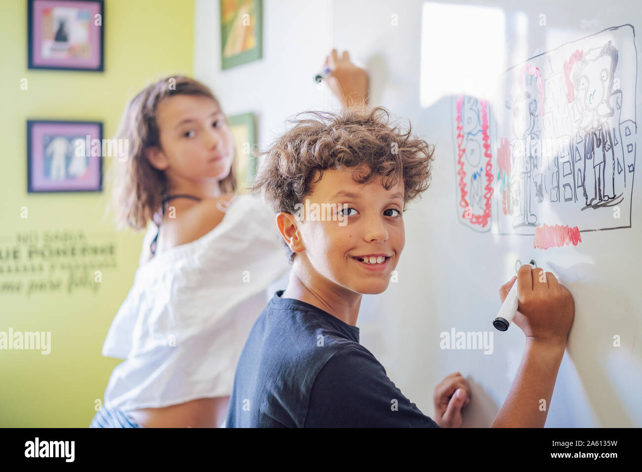 Portrait of smiling boy drawing on a whiteboard with girl in background Stock Photo