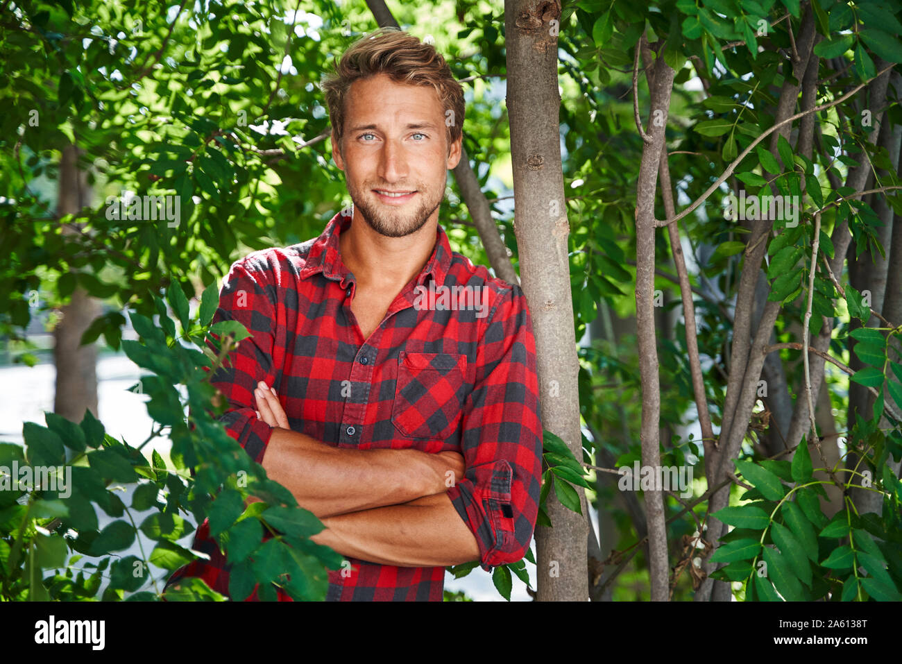 Portrait of confident young man wearing checkered shirt leaning against a tree Stock Photo