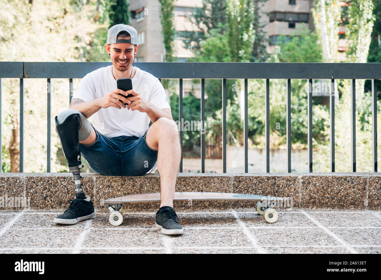 Smiling young man with leg prosthesis and skateboard using smartphone Stock Photo