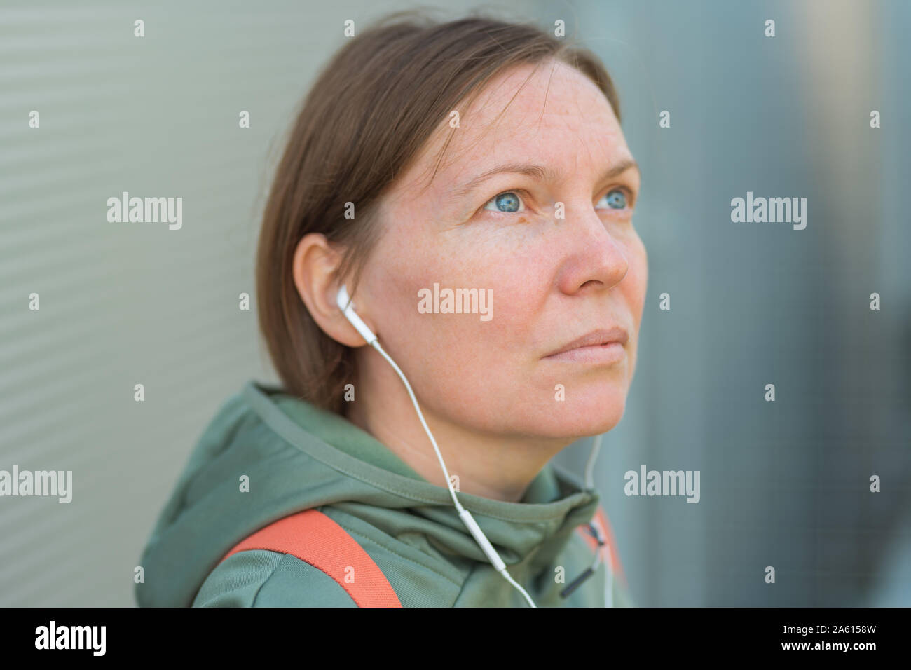 Brisk walker female listening music on earphones, portrait of woman in sports clothing in urban surrounding Stock Photo