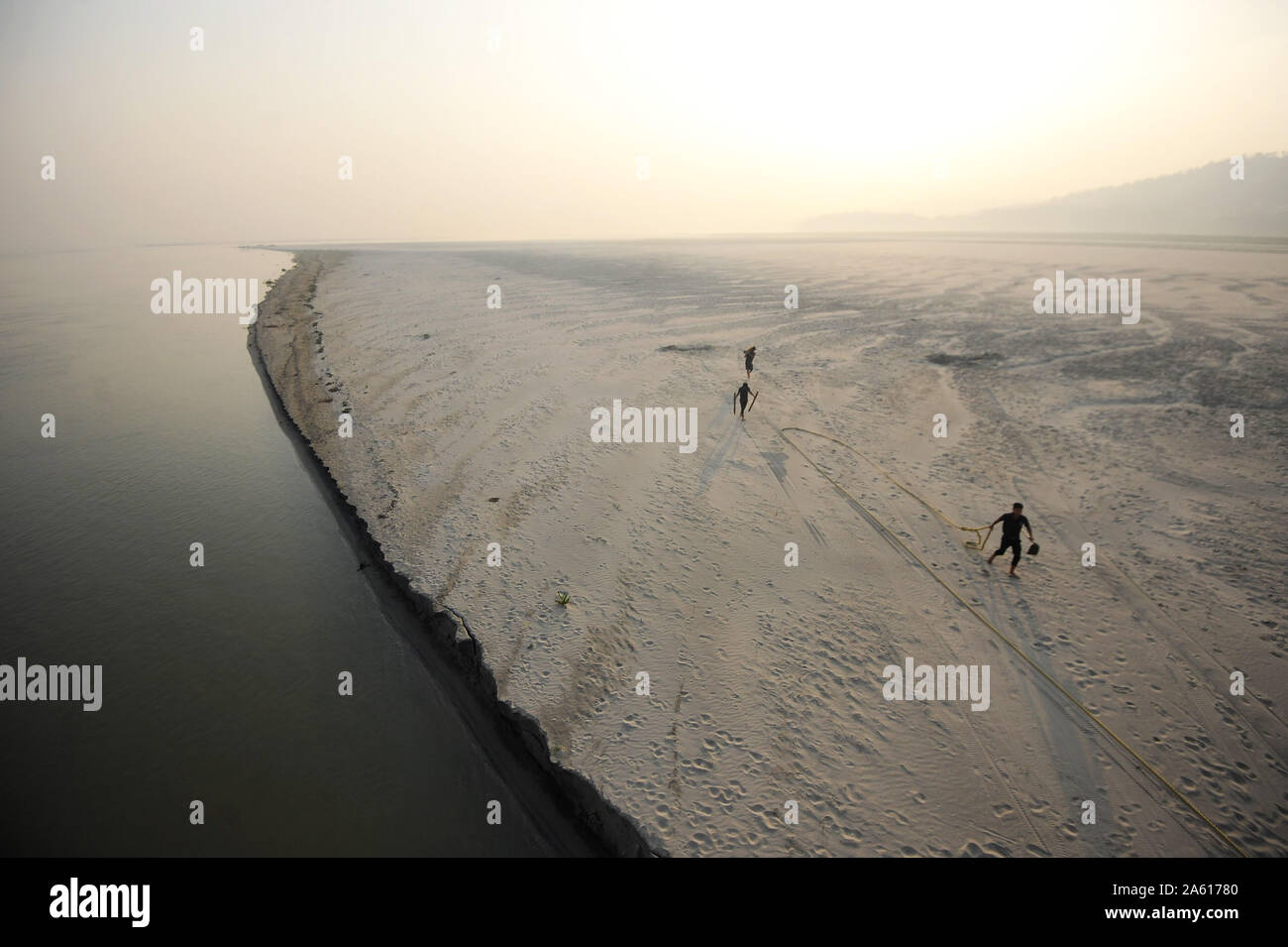 Three men at sunrise releasing ropes from a mooring in the fine sand of a seasonal sandspit, Brahmaputra River, Assam, India, Asia Stock Photo
