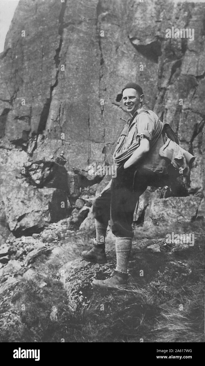Man wearing a pack and holding climbing ropes poses outside with rock face during a Northern Cavern and Fell Club rock climbing and spelunking event in Yorkshire, United Kingdom, 1934. () Stock Photo