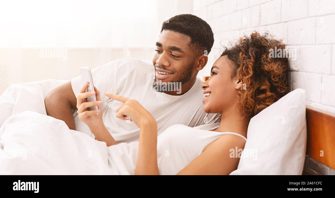 Happy loving black couple networking on cellphones in bed Stock Photo ...
