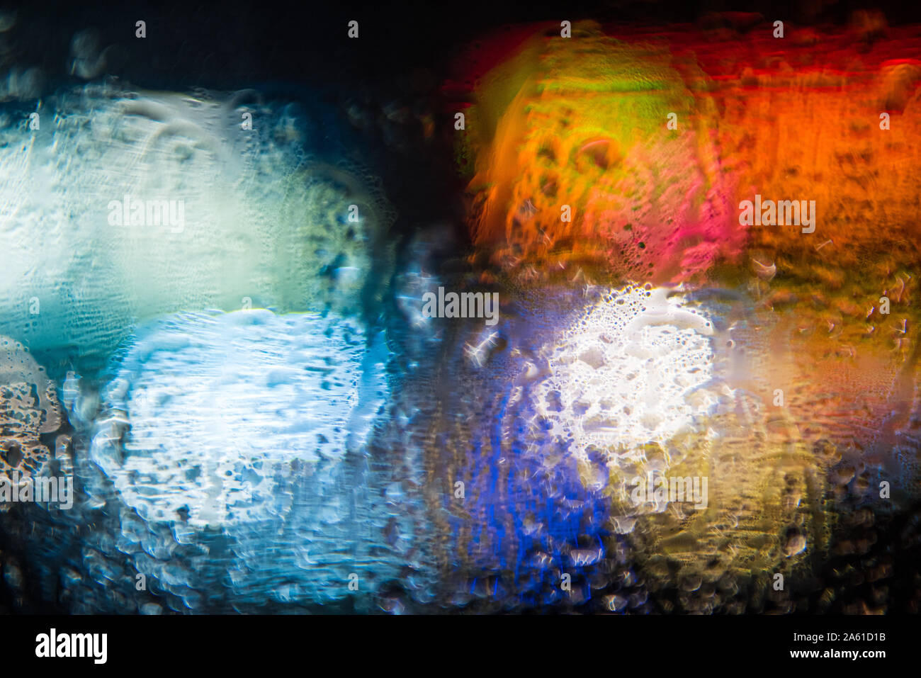 abstract out of focus bold coloured lights shot on the street rain on a car window, high quality good for backgrounds and eye catching advertising. Stock Photo