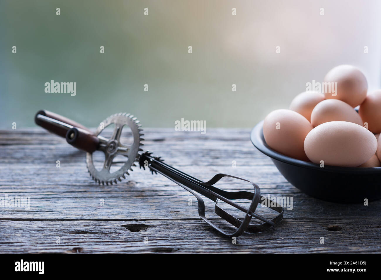 https://c8.alamy.com/comp/2A61D5J/old-egg-whisk-mixer-and-a-bowl-with-organic-eggs-on-the-rustic-weathered-grey-wooden-table-background-selective-focus-horizontal-with-copy-space-2A61D5J.jpg