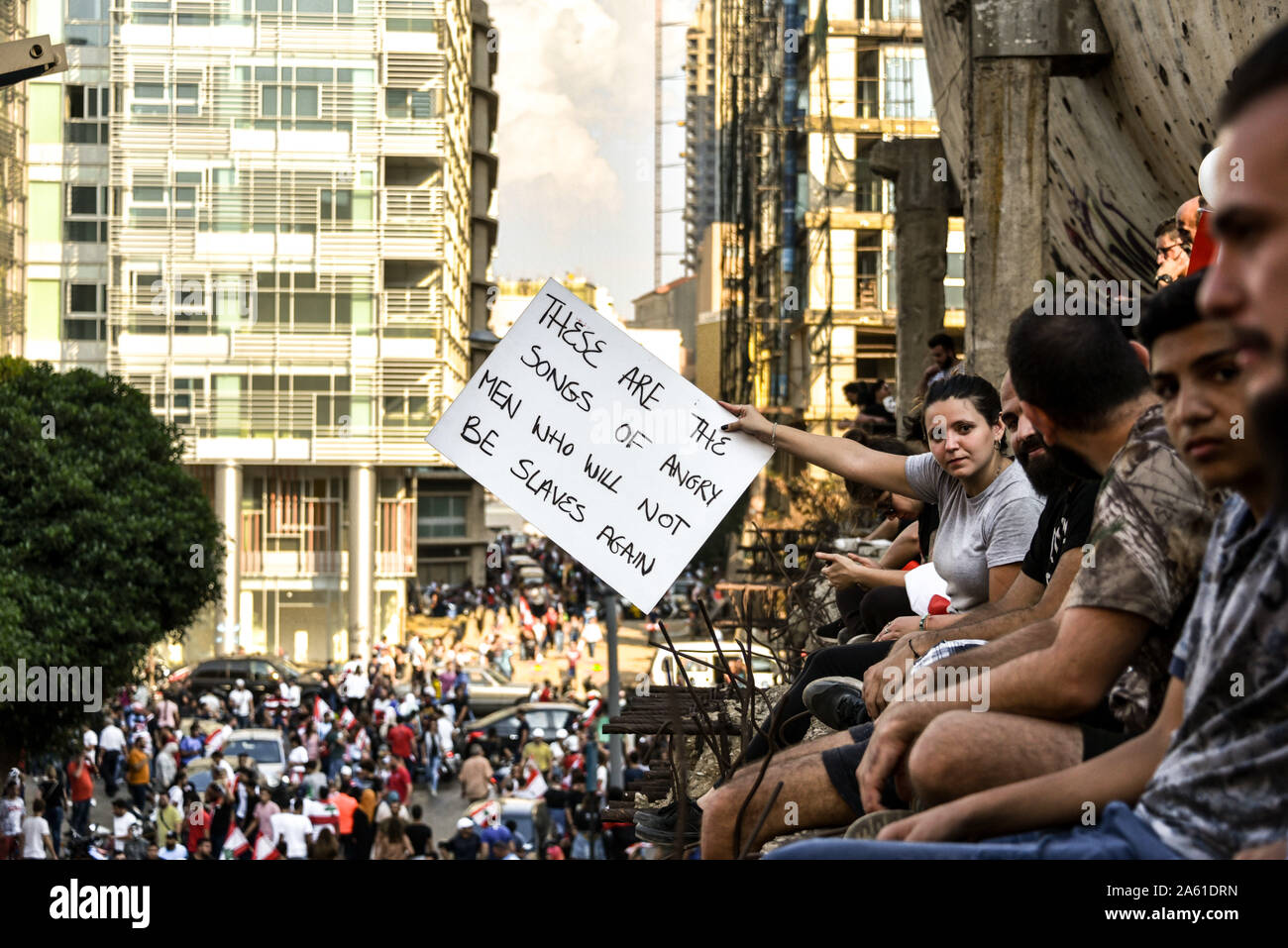 A protester sitting on the iconic Egg building in Downtown Beirut holds out a sign with a quote from Les Mis 'These are the songs of angry men who will not be slaves again'. The people of Lebanon say they will not stop revolting until the entire government has stepped down. Across the country similar mass gatherings have settled in for the long haul as the people come together for a 7th consecutive day. United under one flag, this multi-sect country is calling for an end to its sectarian government and retribution for the corruption it has been subject to for 30 years. Stock Photo