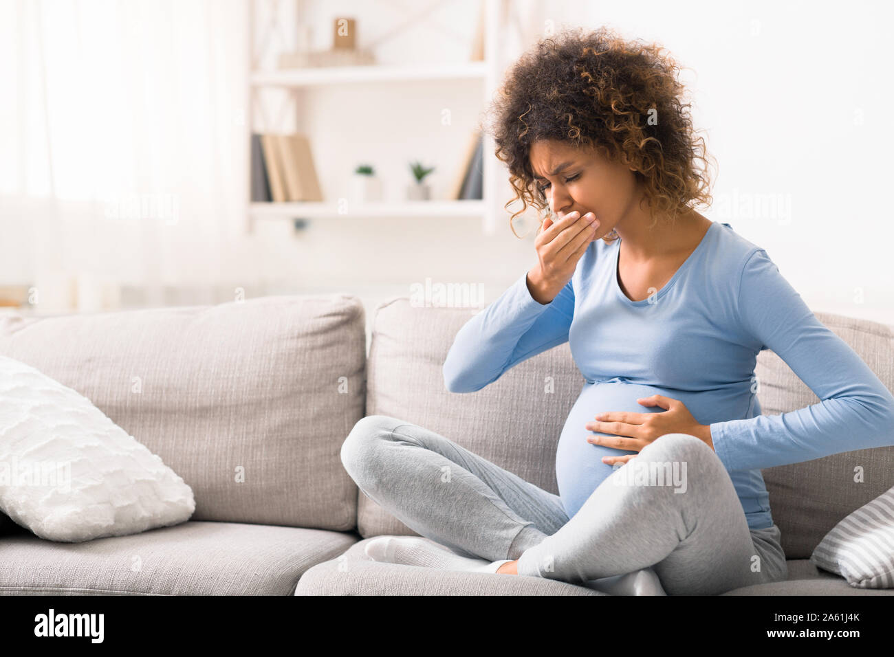 Young pregnant lady suffering with nausea, sitting on sofa Stock Photo