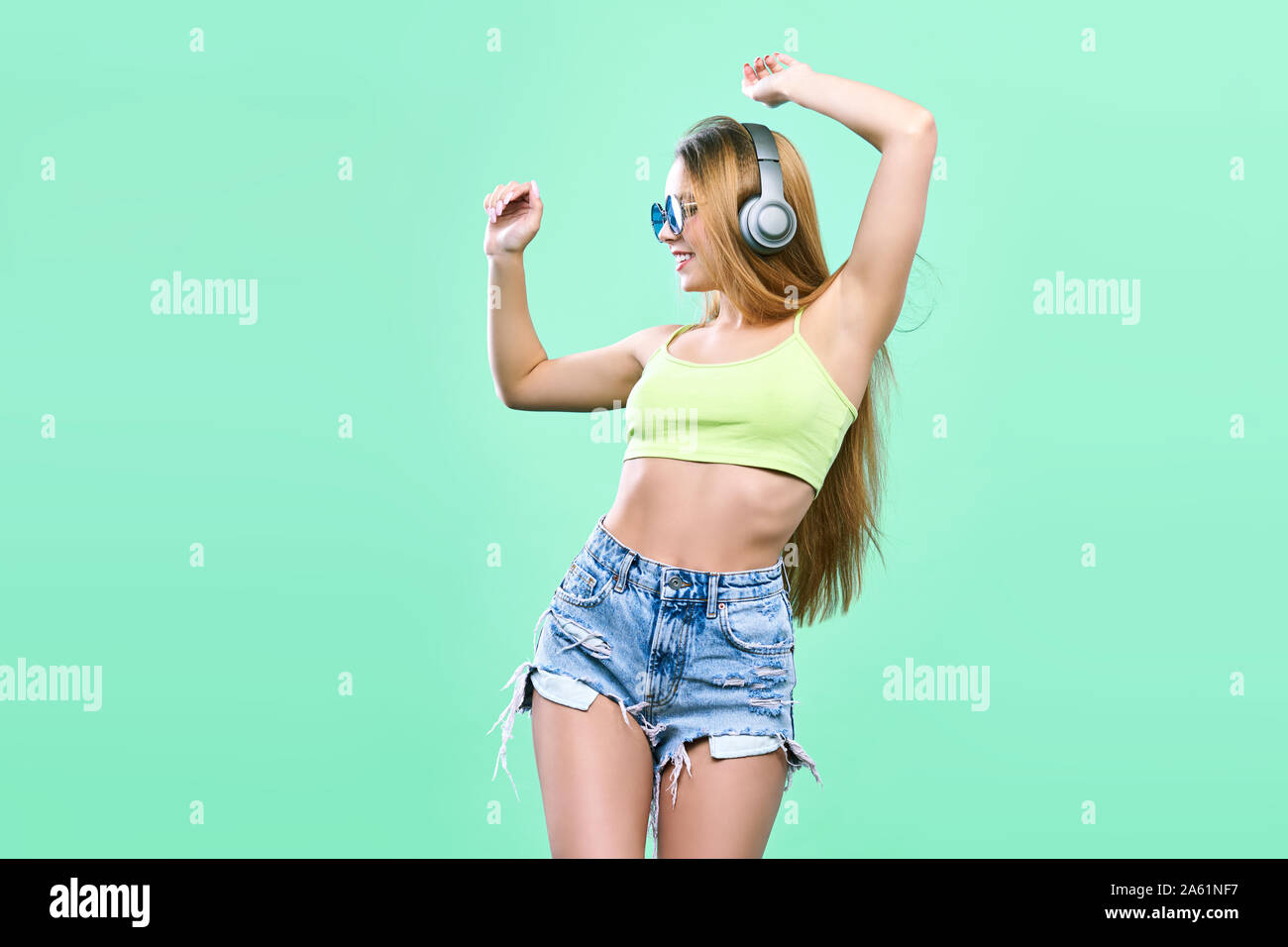 Pretty cool girl having fun and listens to music in the headphones on smartphone over colorful background. Stock Photo