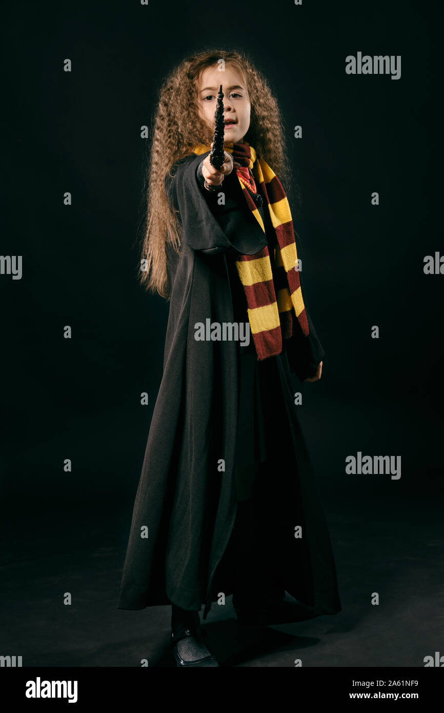 Portrait of a charming enchantress child with magnificent long brown hair dressed in a dark coat, yellow and burgundy striped scarf, gray skirt, knee Stock Photo