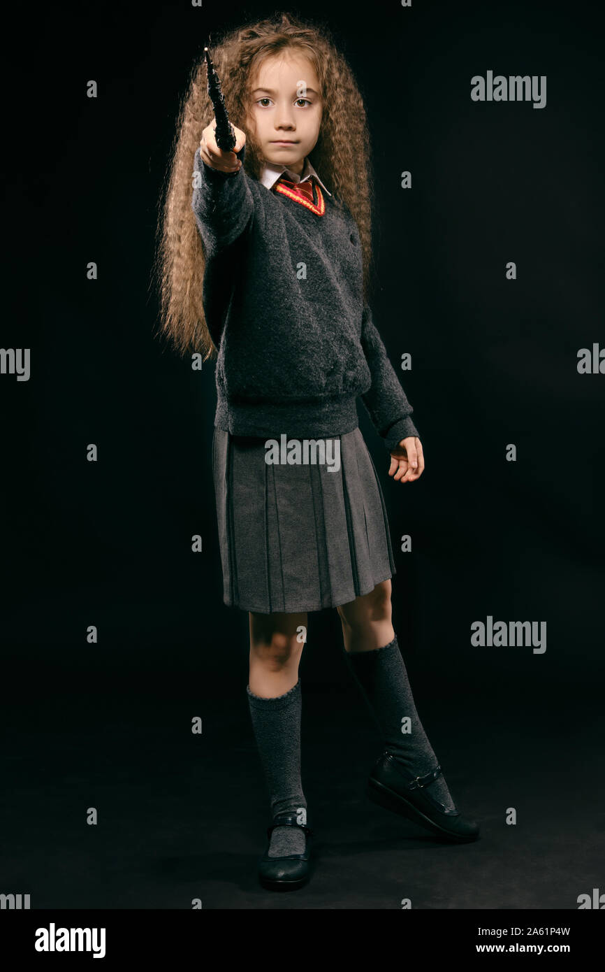 Portrait of a beautiful enchantress child with magnificent long brown hair dressed in a navy blue jumper, gray skirt, knee socks and shoes. She is hol Stock Photo