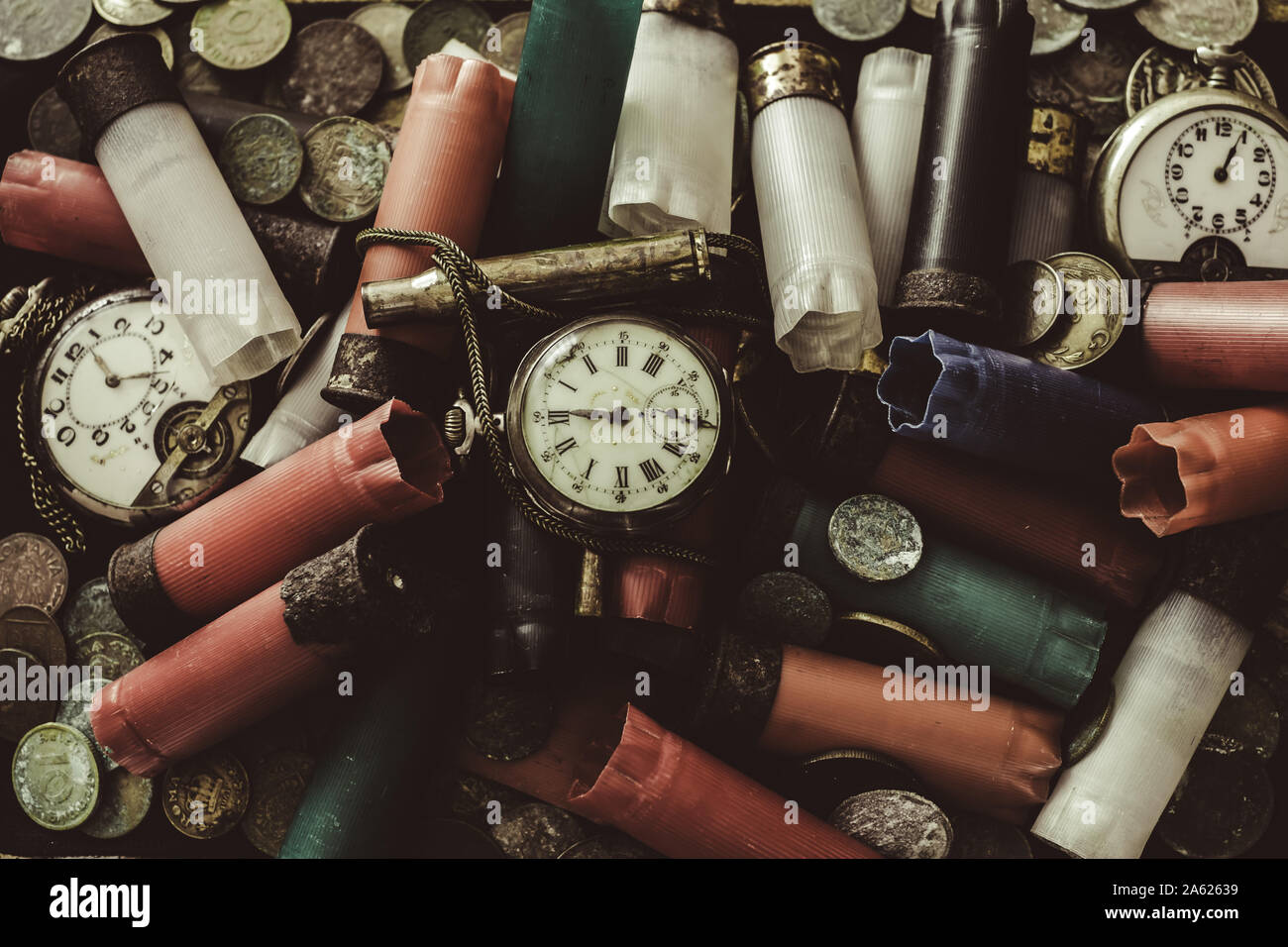 A disordered pile of old objects on the desk, hunting cartridges used, broken pocket watches, old coins, old banknotes and little chains Stock Photo