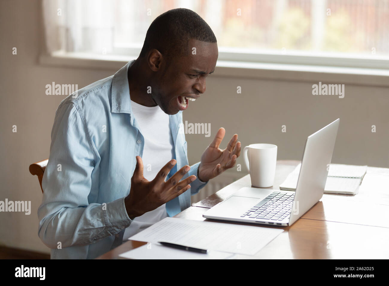 Stressed millennial african ethnic guy irritated by broken computer. Stock Photo