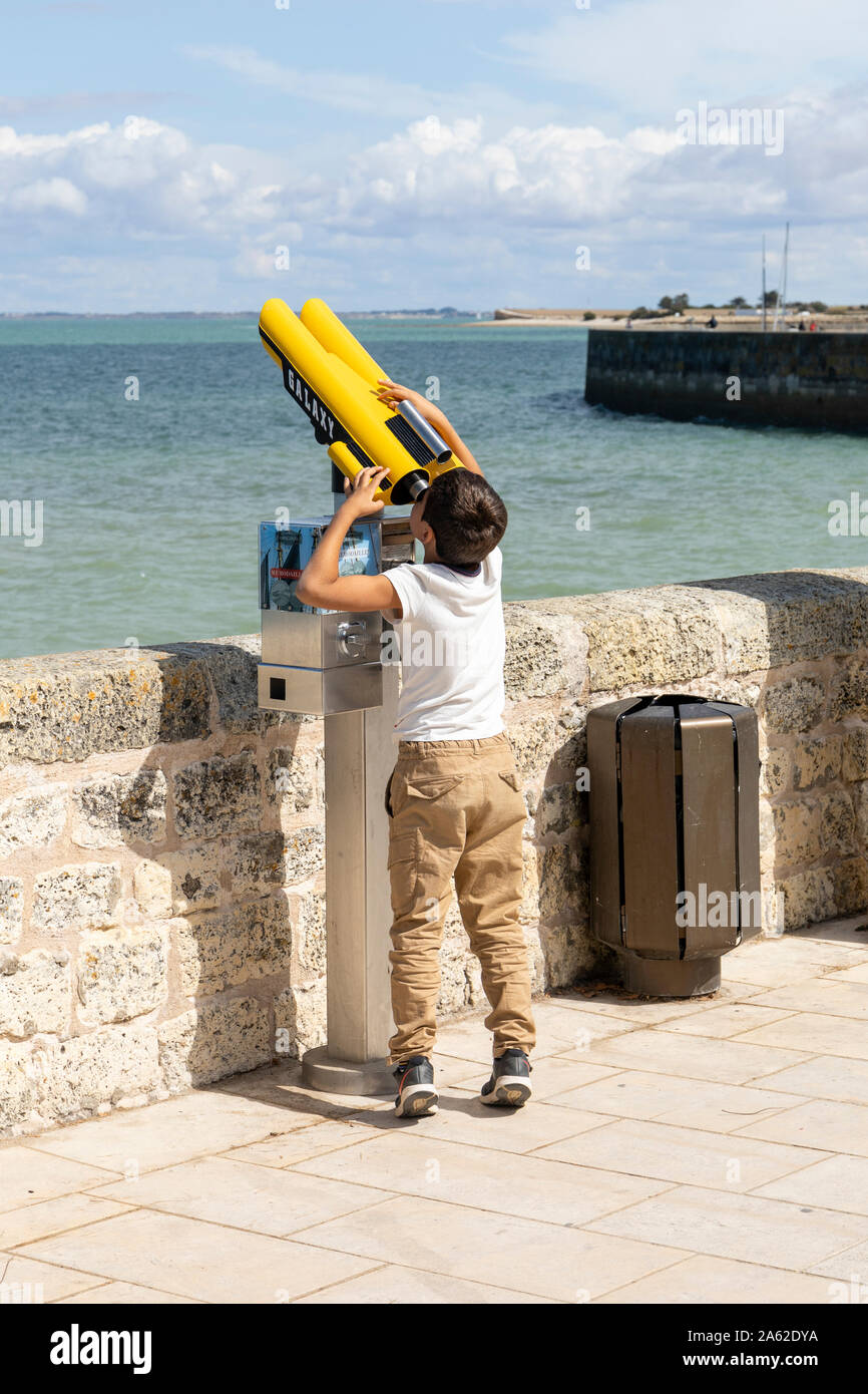 A boy strains to see through a telescope on the sea front at La Flotte, Ile de Re, France Stock Photo