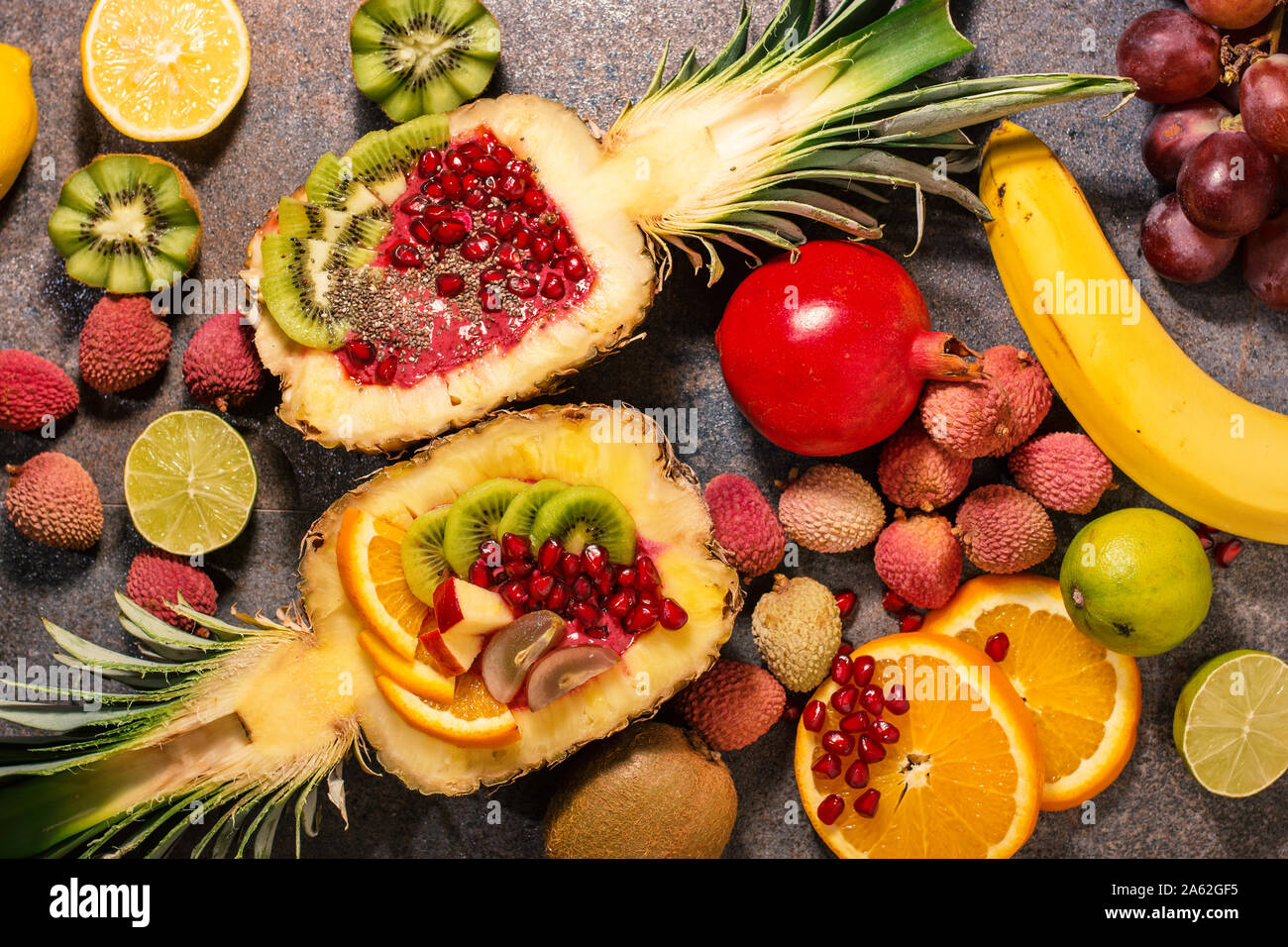 Cut in half pineapple, lying flat in composition with other fruits. A midd filled with homemade ice cream from healthy, fresh forest fruits. Stock Photo