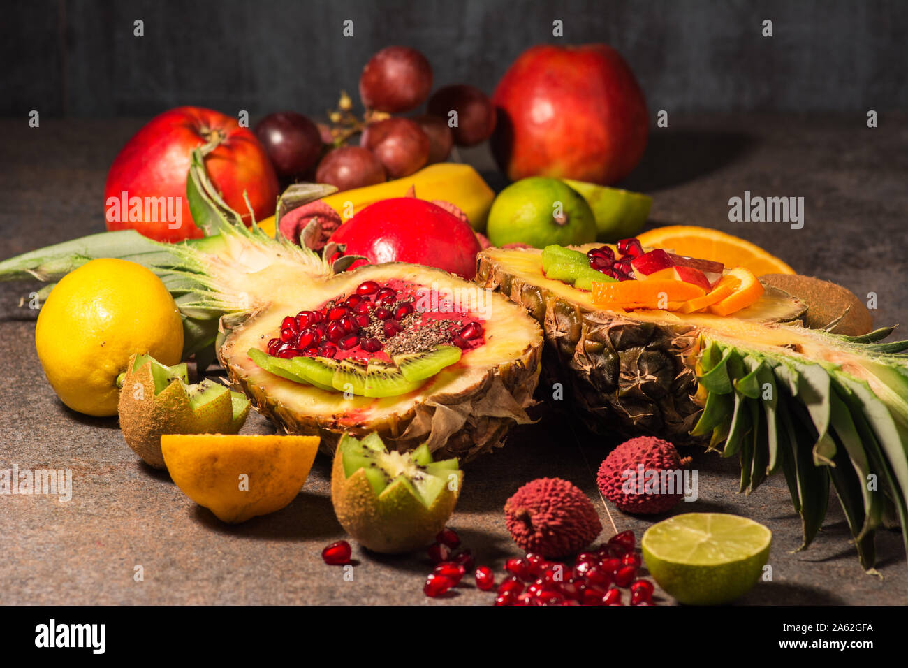 Cut in half pineapple, lying flat in composition with other fruits. A midd filled with homemade ice cream from healthy, fresh forest fruits. Stock Photo