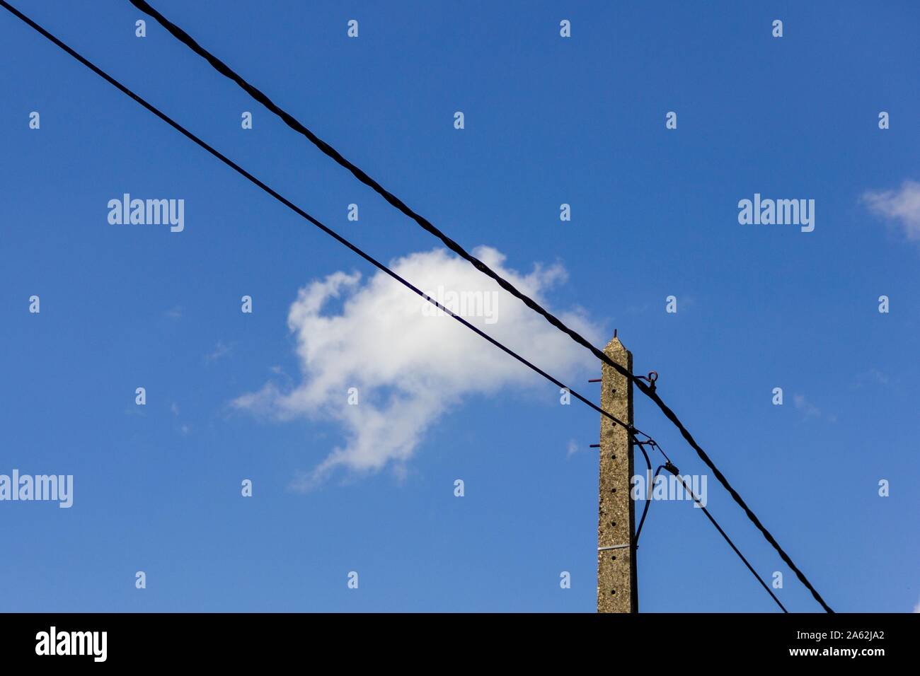 A portrait of an electric pole with electric wires in a blue sky with a ...