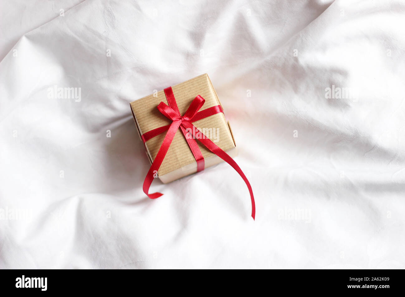 Present Box Wrapped in Kraft Paper Decorated with Red Ribbon Bow. Festive Christmas Gifts Wrapping. Stock Photo