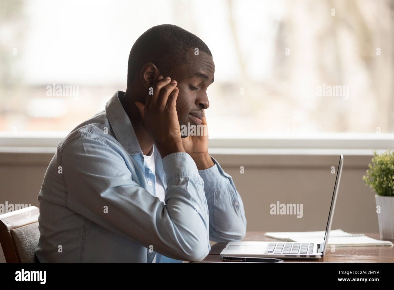 Overwhelmed exhausted young african american guy suffering from headache. Stock Photo