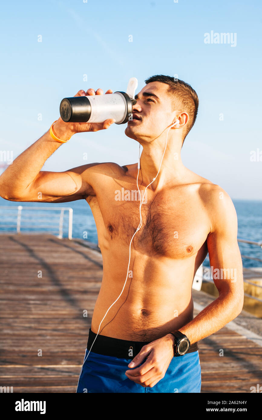 Fit man using his phone whilst drinking water after hard workout. Stock Photo