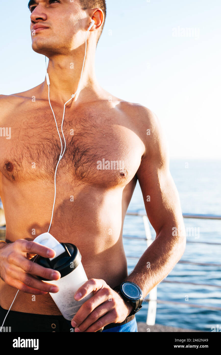 sportsman with muscular body holding water bottle against a blue sky background Stock Photo