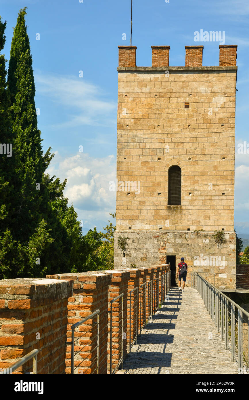 View of the elevated walkway on the ancient city walls of Pisa with a corner tower and a tourist walking from behind in summer, Tuscany, Italy Stock Photo