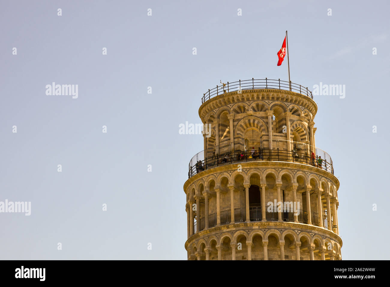 Upper part of the famous Leaning Tower in Piazza dei Miracoli of Pisa with tourists on the top terrace against blue sky background, Tuscany, Italy Stock Photo