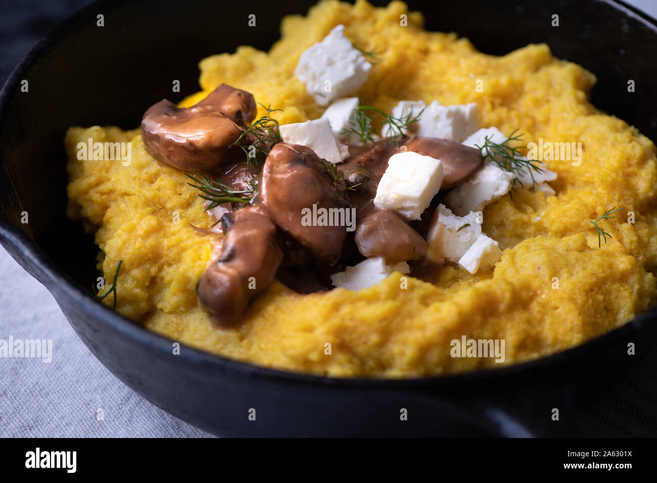 Traditional Eastern European corn mush (mamaliga, polenta, banosh, balmes) topped with sheep cheese, mushroom gravy, fried meat pieces Stock Photo