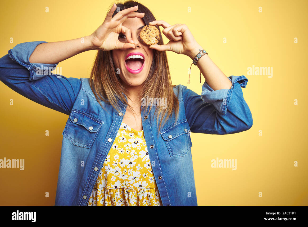 Young beautiful woman eating chocolate chips cookie over yellow ...