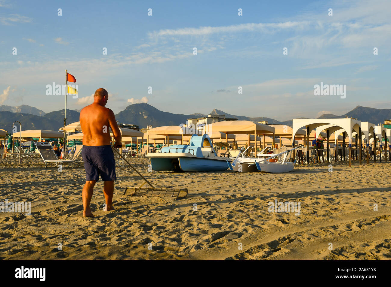 A mature man from behind raking the sand of a beach in Lido di Camaiore on the Versilia coast at sunset in summer, Tuscany, Italy Stock Photo
