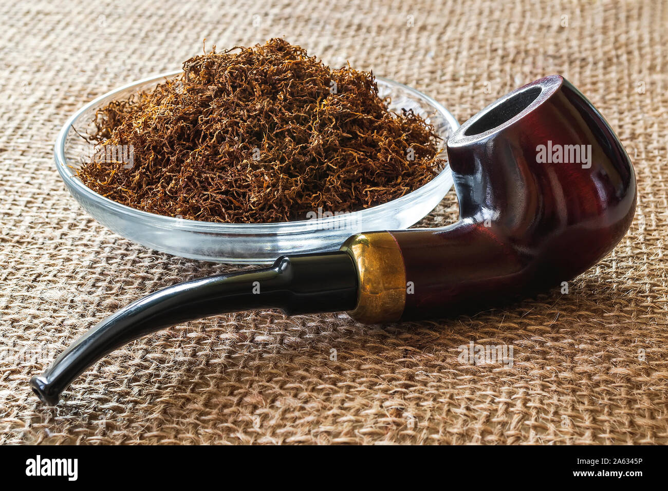 Wooden pipe near heap of tobacco in a glass bowl on a sackcloth