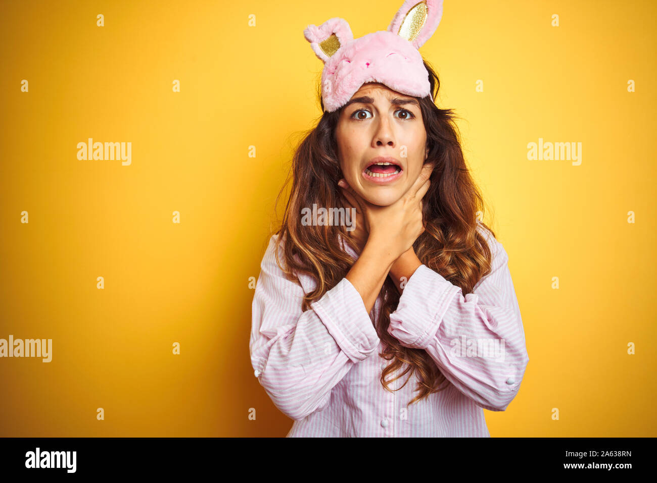 Young woman wearing pajama and sleep mask standing over yellow isolated