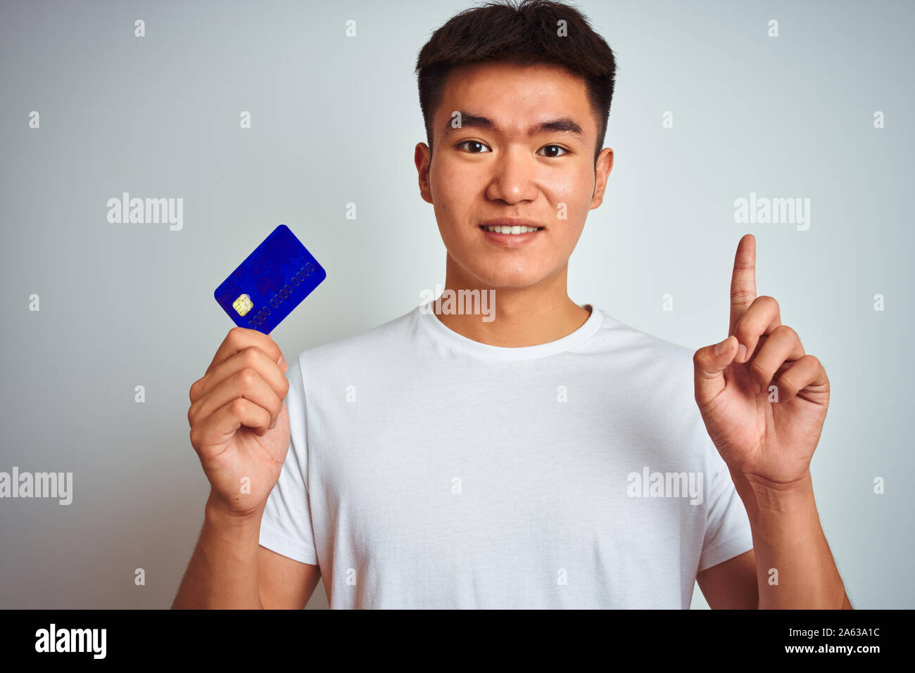 Young asian chinese man holding credit card standing over isolated ...