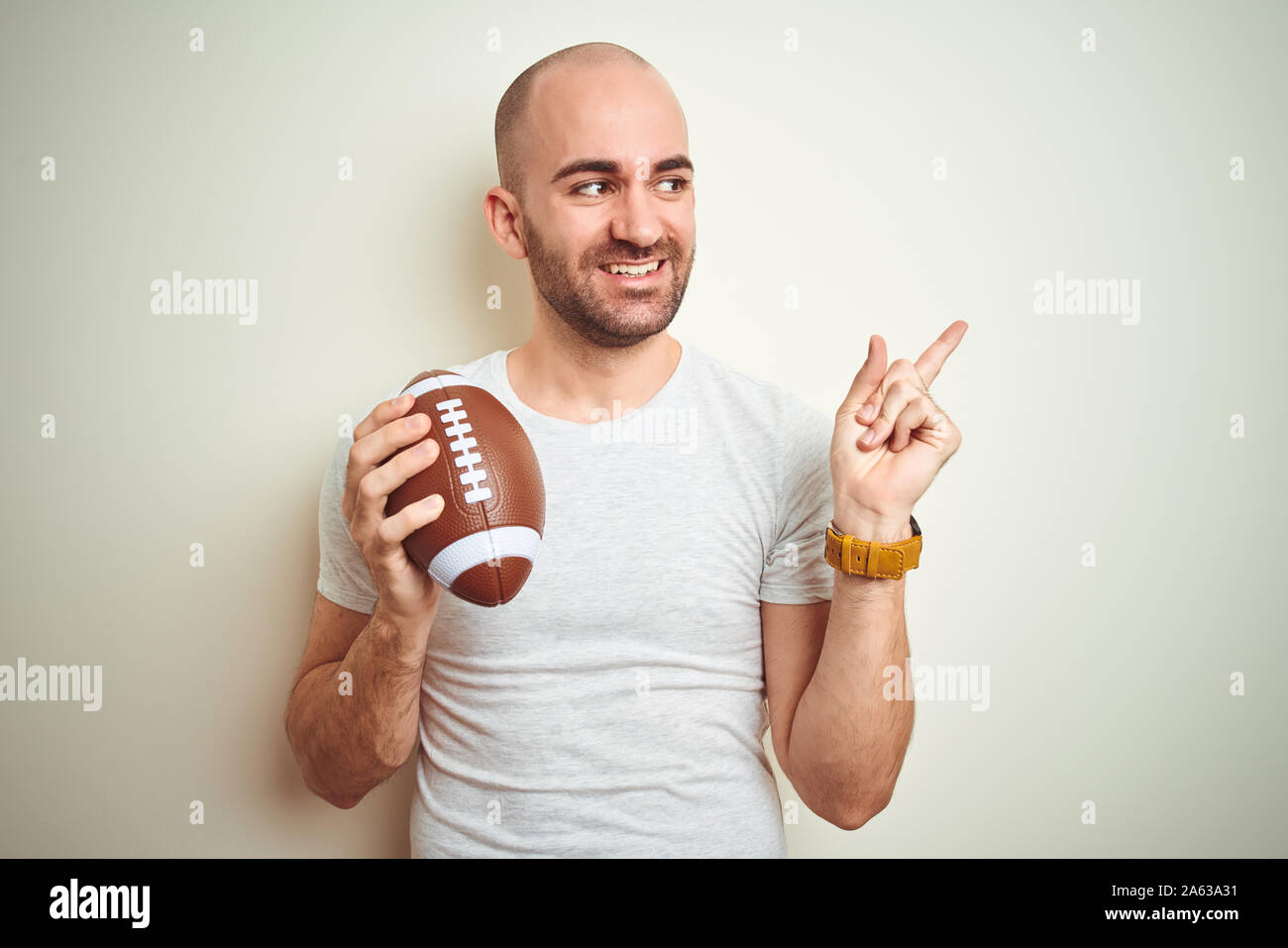 Young man holding rugby american football ball over isolated background very happy pointing with hand and finger to the side Stock Photo