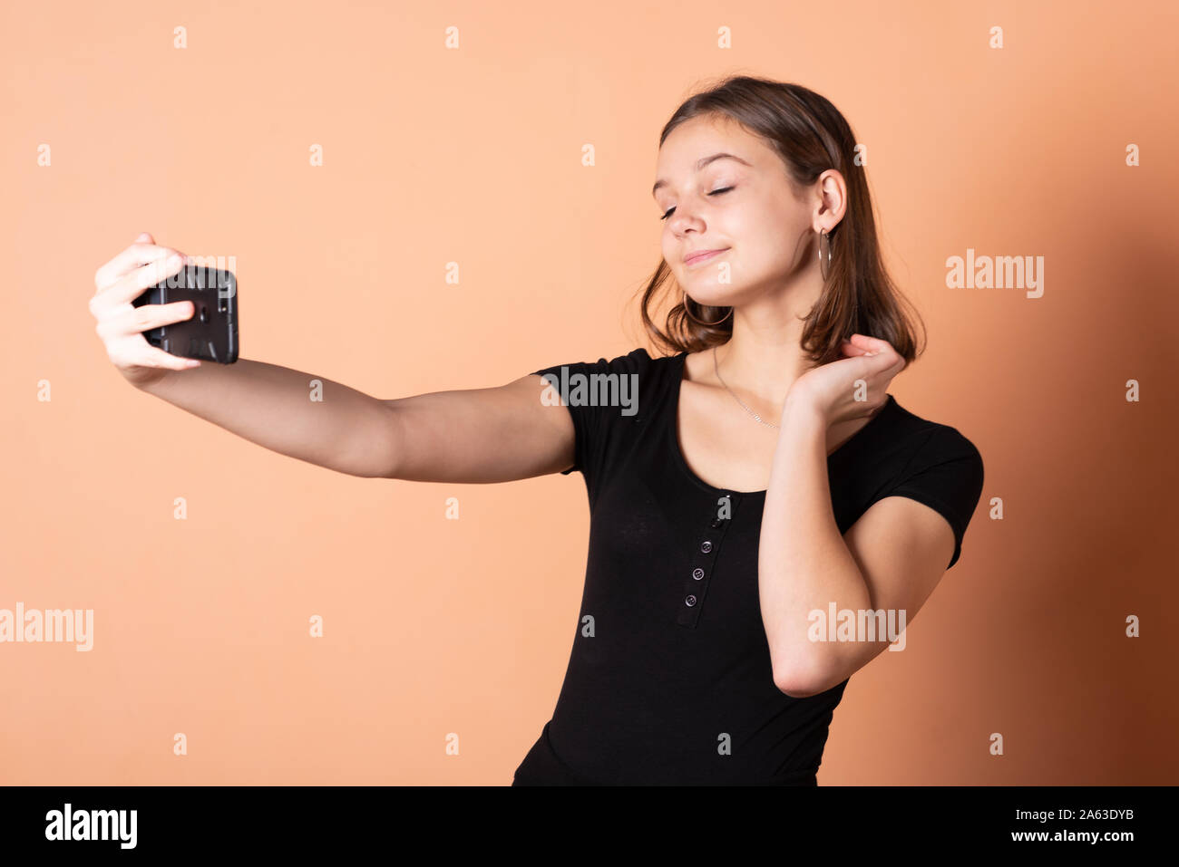 Little girl takes a selfie, on a light orange background. Stock Photo