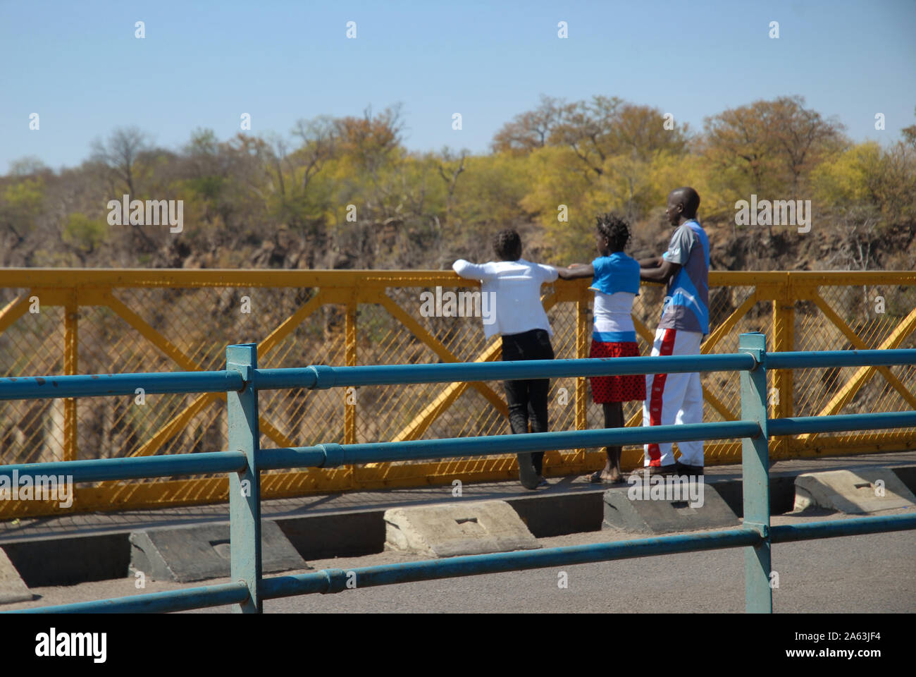 Three people looking over edge of Victoria Falls Bridge, Zimbabwe, Africa. Stock Photo