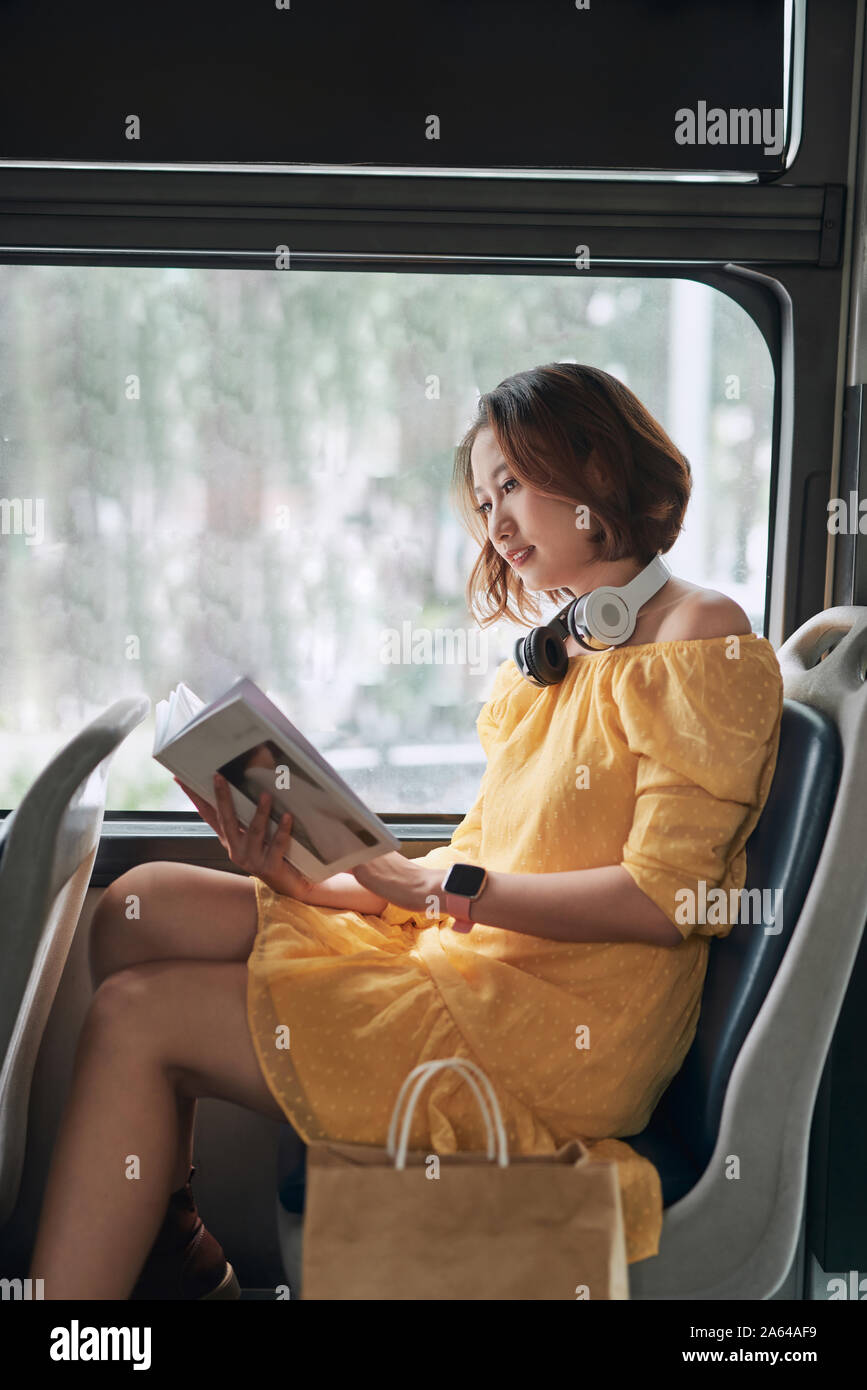 Young woman reading book while moving in the modern tram, happy passenger at the public transport Stock Photo