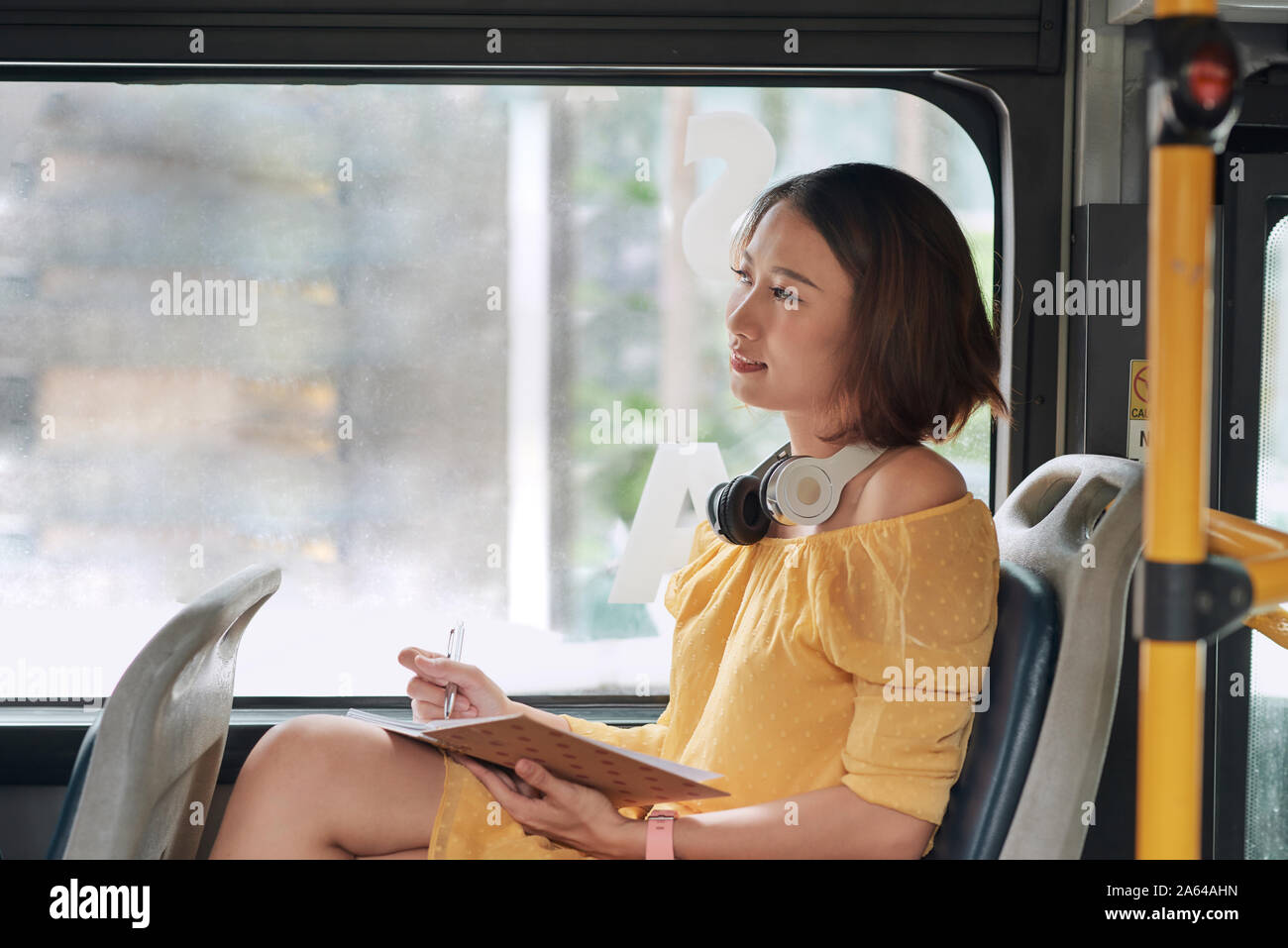 Beautiful young woman sitting in city bus and writing some notes in notebook. Stock Photo
