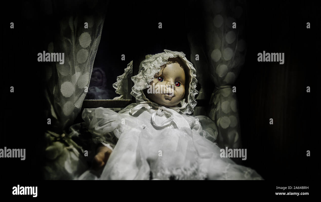 horror vintage baby girl doll with scar face sit against the window, black vignette border effect for Halloween background Stock Photo