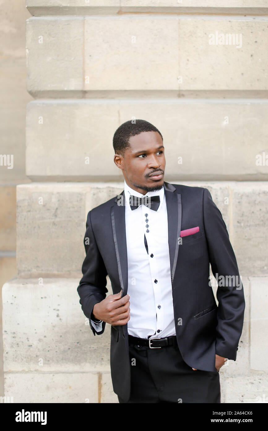 Afro american successful man wearing dark suit and standing near wall ...