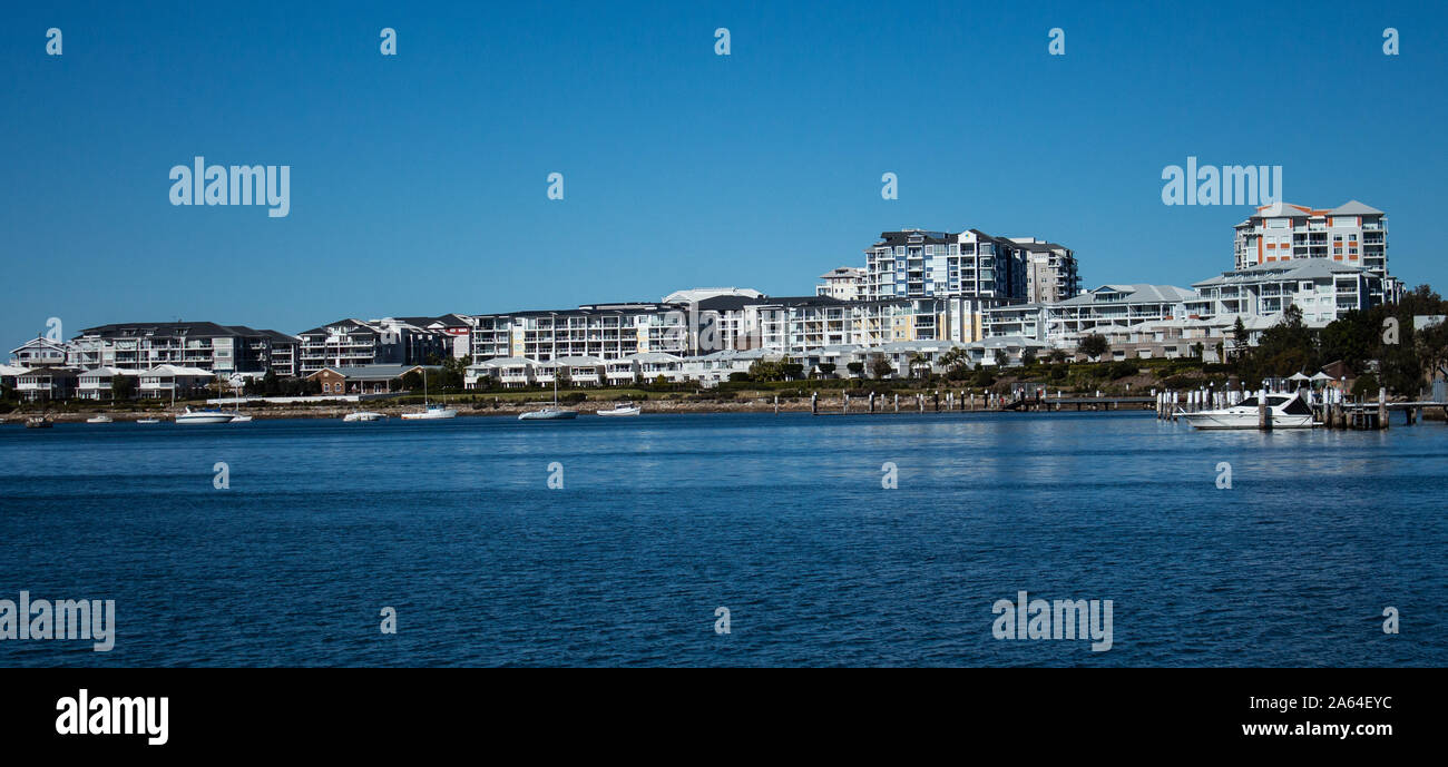 Large waterside houses, apartment condominiums in suburban community on riverfront with boats moored at wharf, blue sky in background Stock Photo