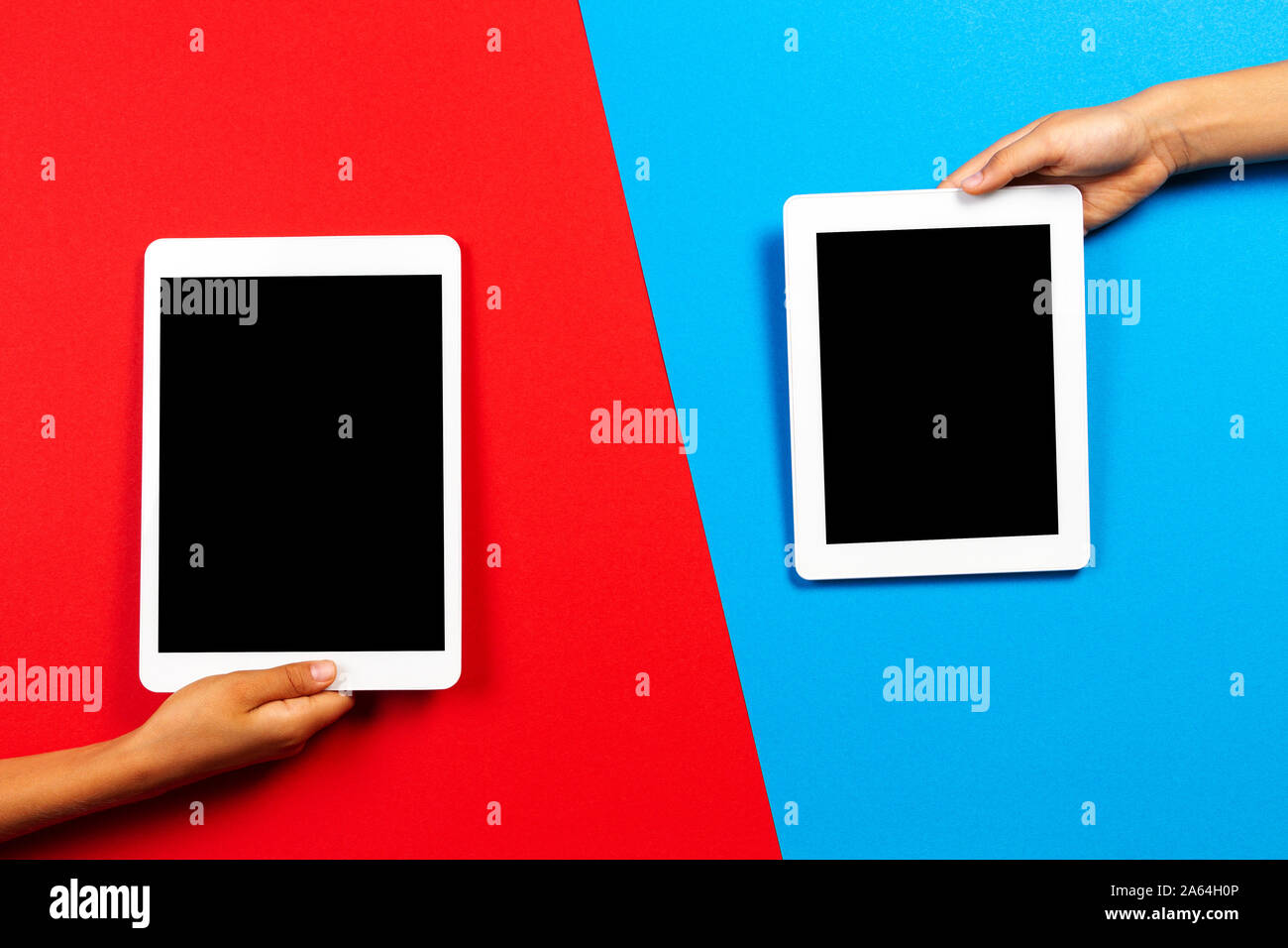 Kids hands holding tablet computer over red and light blue background Stock Photo