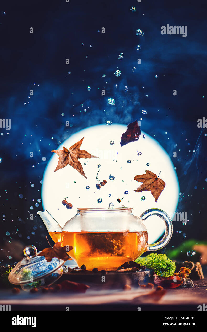 Autumn tea in glass teapot with shining full Moon, falling leaves and water drops. Creative drink photography concept Stock Photo