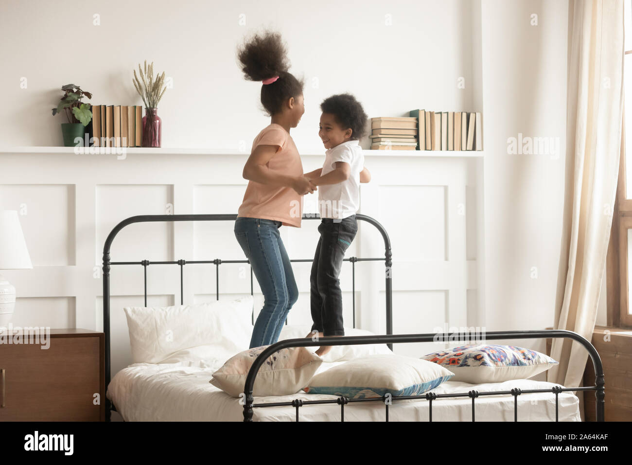 Active black brother and sister jump on bed together Stock Photo
