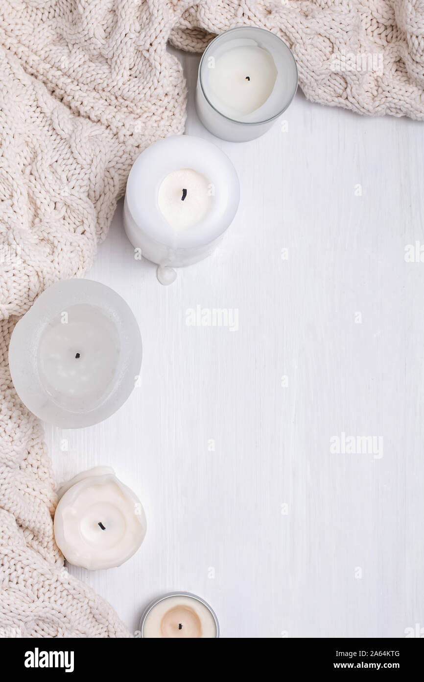 Creative composition with white candles and knitted sweater on the white wooden table Stock Photo