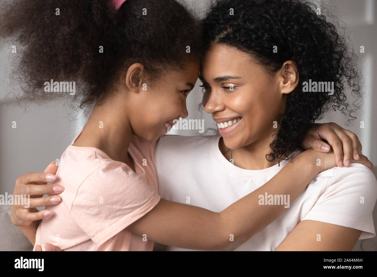 Smiling black mother and daughter look in eyes hugging Stock Photo
