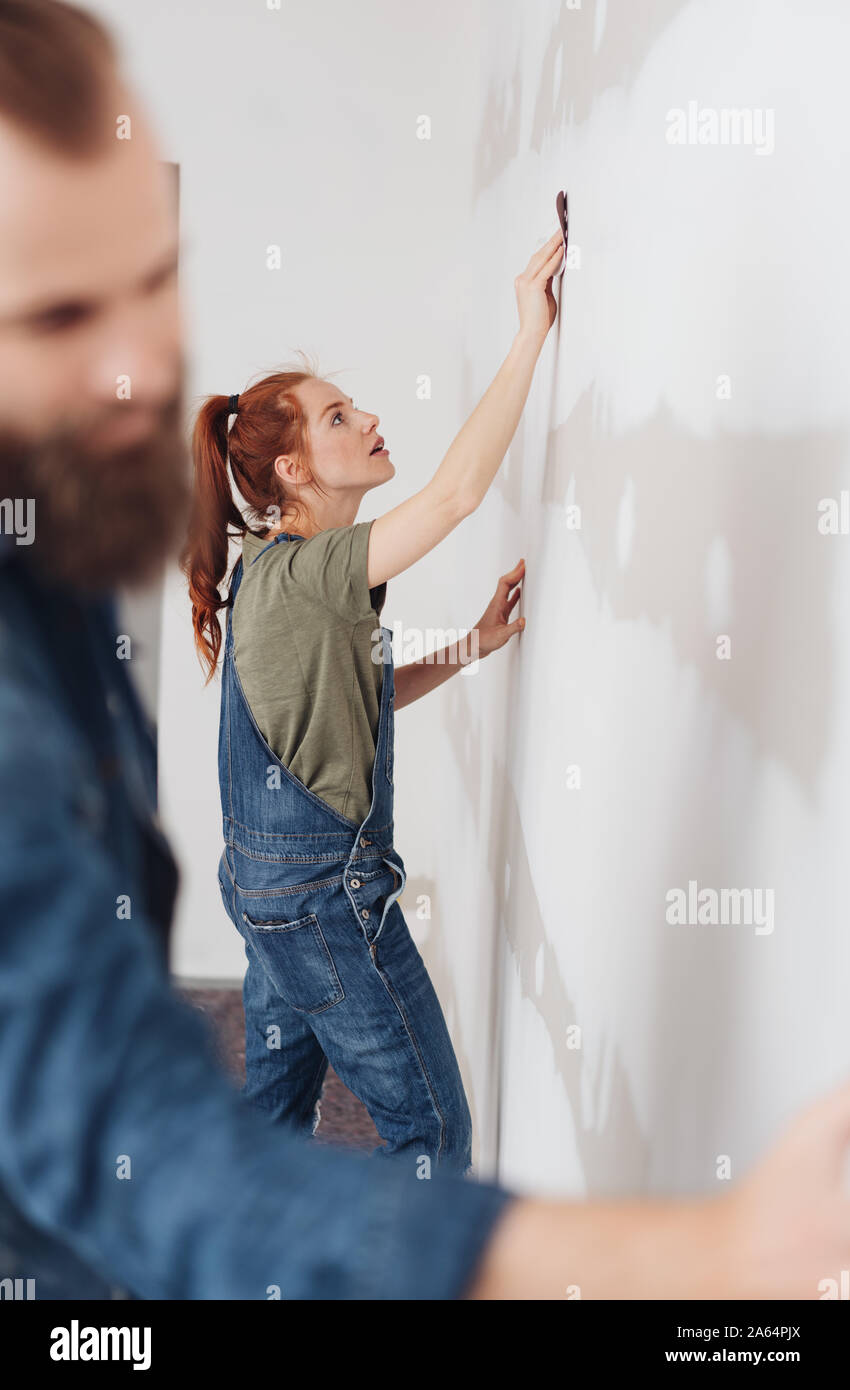 Young Couple Sanding Down A Wall Before Painting During Diy