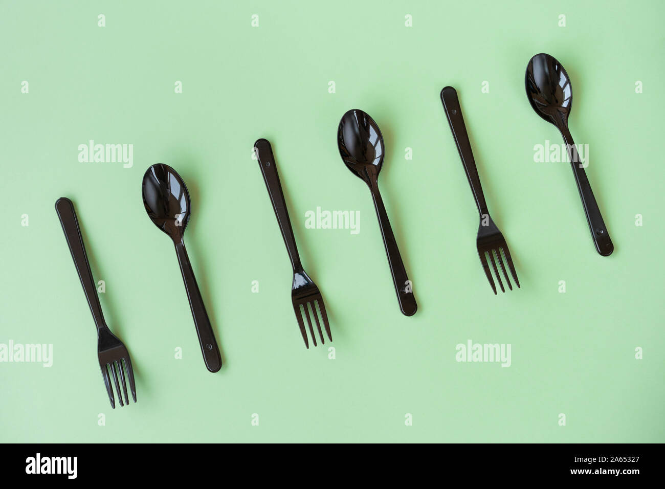 Black plastic spoons and forks lay on a green background in neo light