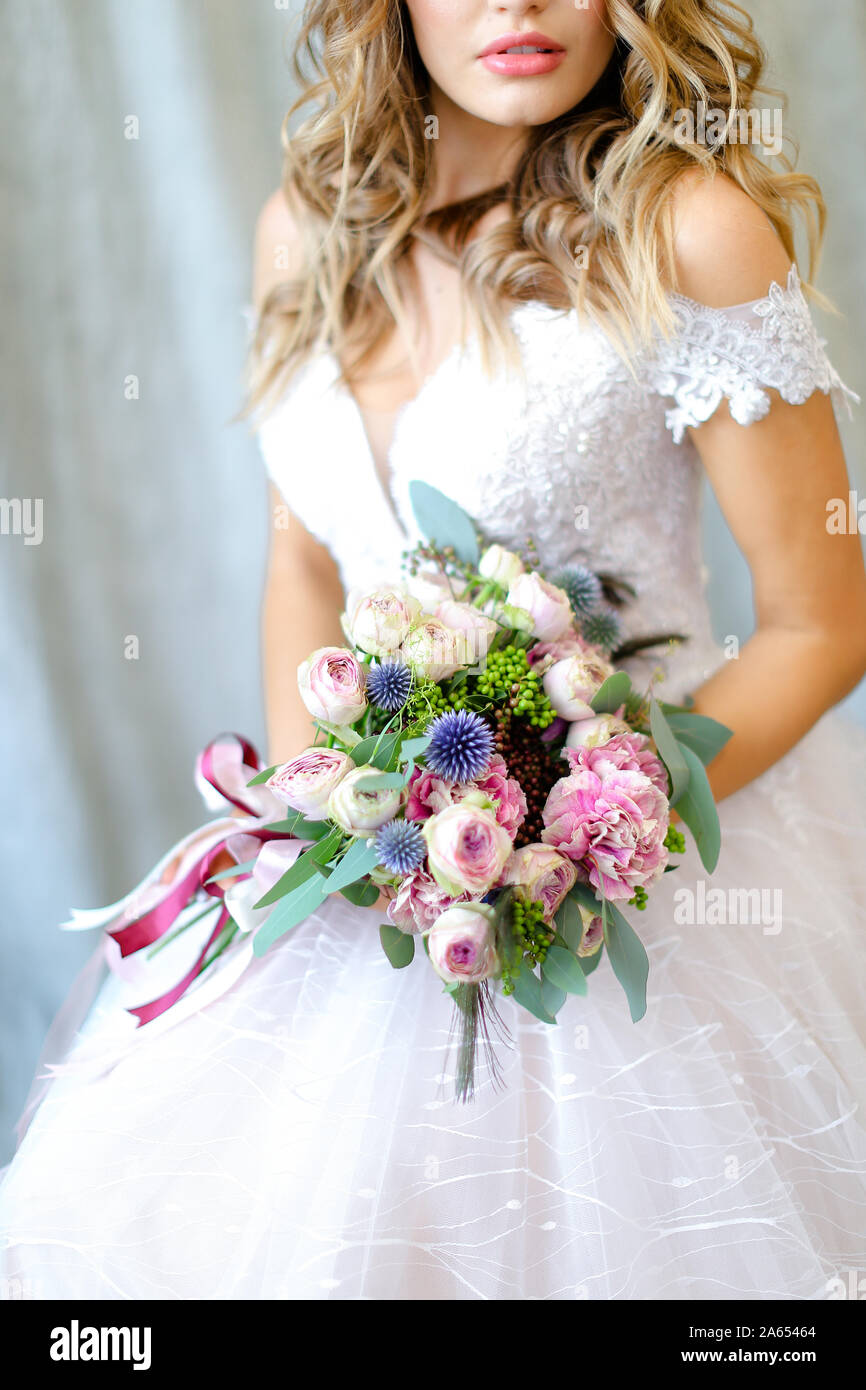 Young bride wearing white dress with bouquet at photo studio. Stock Photo