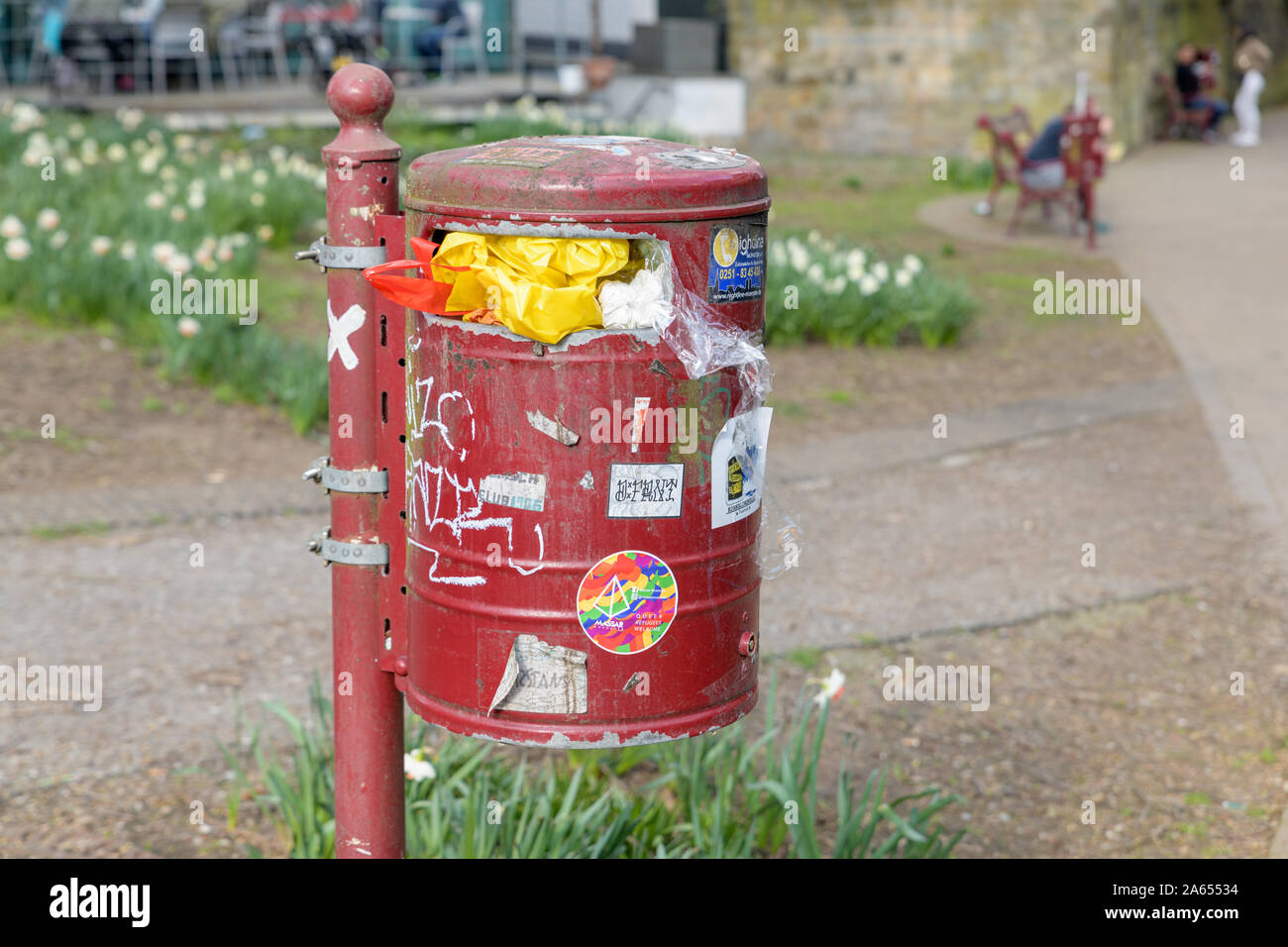 MUENSTER, GERMANY - MARCH 30, 2019: A garbage bin full of waste and covered with stickers and messages stands in a park in Muenster, Germany on March Stock Photo